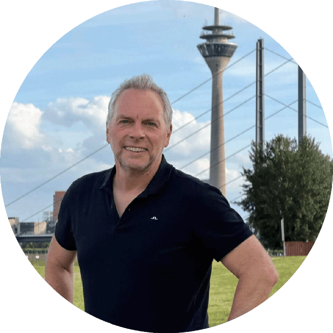 René Dörnenburg – der Gründer vom Onlineshop 88miles.shop – steht auf den Rheinweisen in Düsseldorf mit Rheinturm im Hintergrund